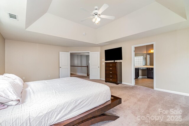 bedroom featuring connected bathroom, a tray ceiling, light colored carpet, visible vents, and baseboards