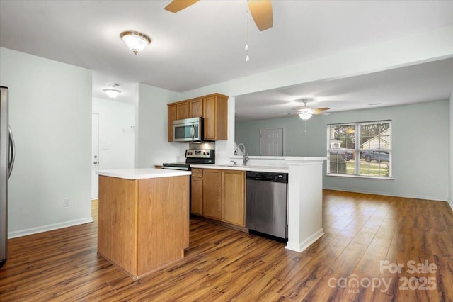 kitchen featuring light countertops, a kitchen island, appliances with stainless steel finishes, dark wood finished floors, and ceiling fan