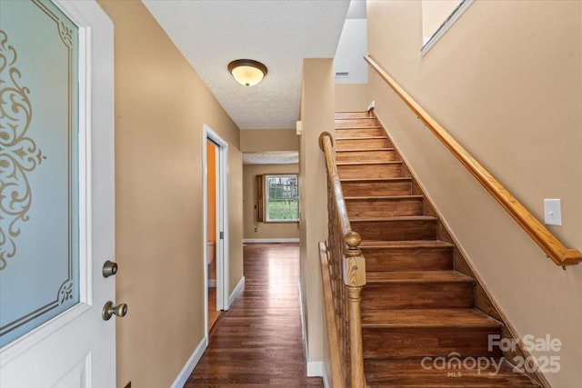 stairway with baseboards, wood finished floors, and a textured ceiling