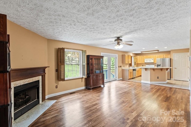 unfurnished living room with a premium fireplace, light wood-style floors, baseboards, and a ceiling fan