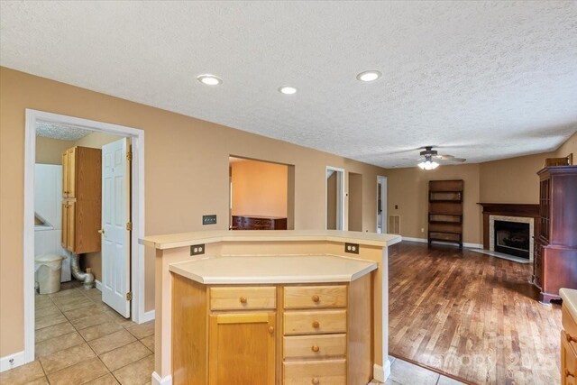 kitchen with light countertops, ceiling fan, a fireplace with flush hearth, and a textured ceiling