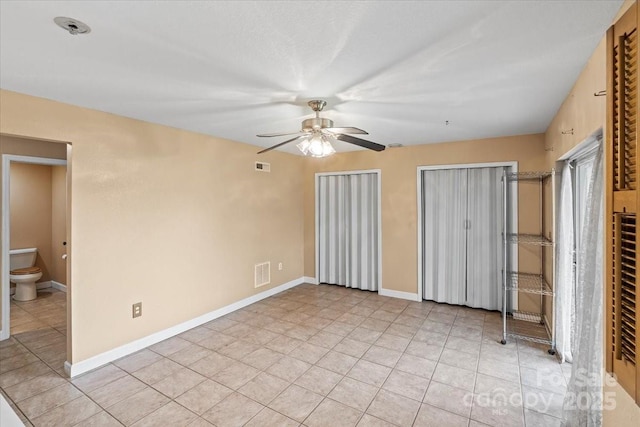 unfurnished bedroom featuring light tile patterned floors, visible vents, baseboards, and ceiling fan