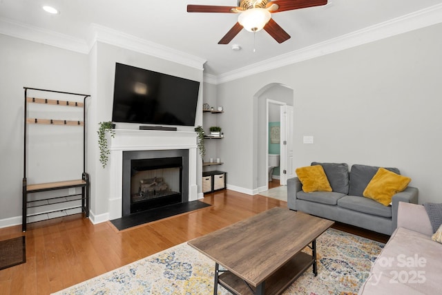 living room with arched walkways, a ceiling fan, crown molding, and wood finished floors