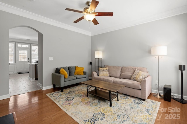 living area with arched walkways, baseboards, a ceiling fan, and crown molding