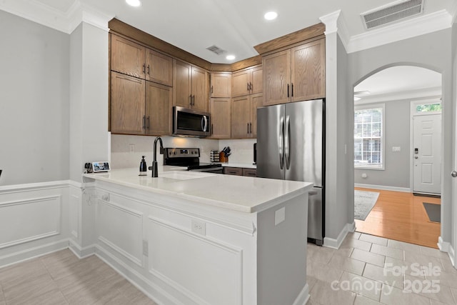 kitchen with ornamental molding, a peninsula, visible vents, stainless steel appliances, and arched walkways