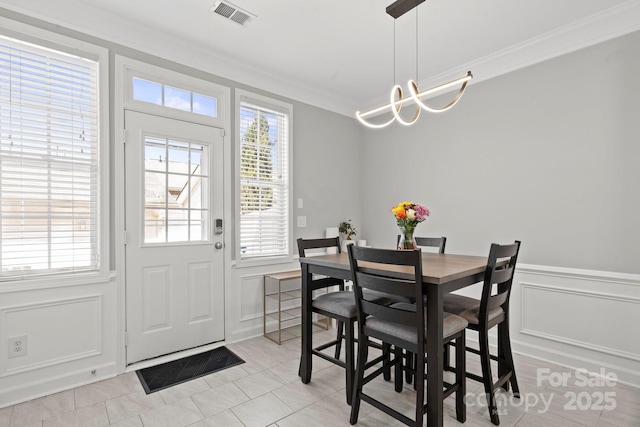 dining room with crown molding, a decorative wall, light tile patterned floors, an inviting chandelier, and visible vents