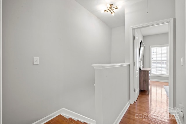 corridor with wood finished floors, baseboards, and an upstairs landing