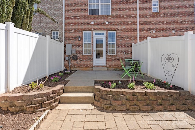 view of exterior entry with brick siding, fence, and a patio area