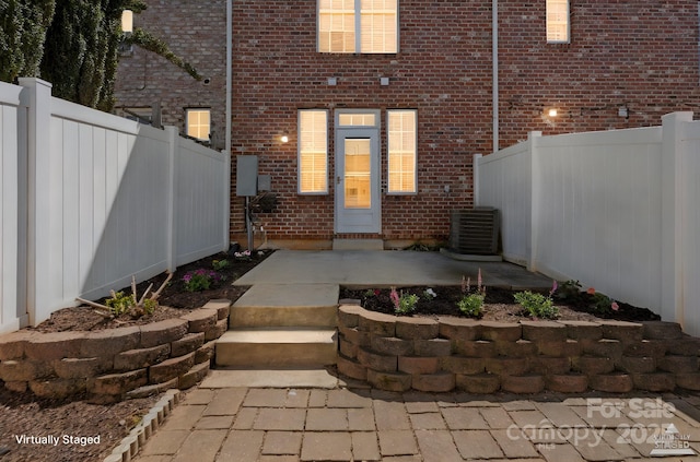 doorway to property featuring brick siding, fence, central air condition unit, and a patio area