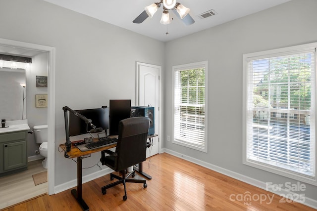 office featuring light wood-style flooring, a ceiling fan, visible vents, a sink, and baseboards