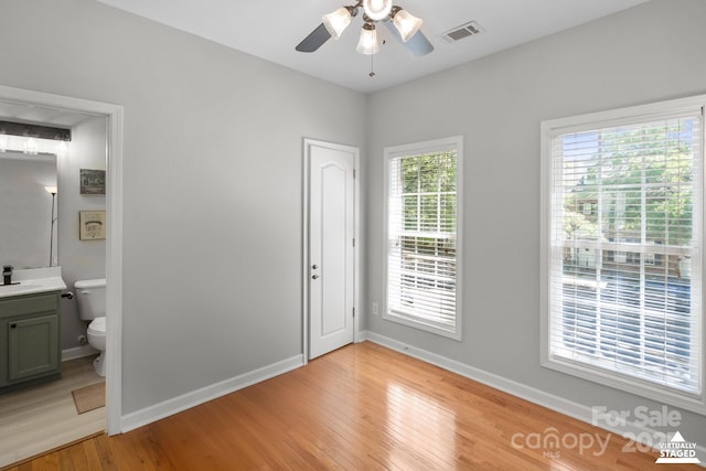 unfurnished bedroom with visible vents, baseboards, a sink, light wood-style floors, and connected bathroom
