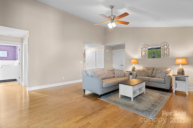 living area featuring light wood-style floors, baseboards, a ceiling fan, and high vaulted ceiling