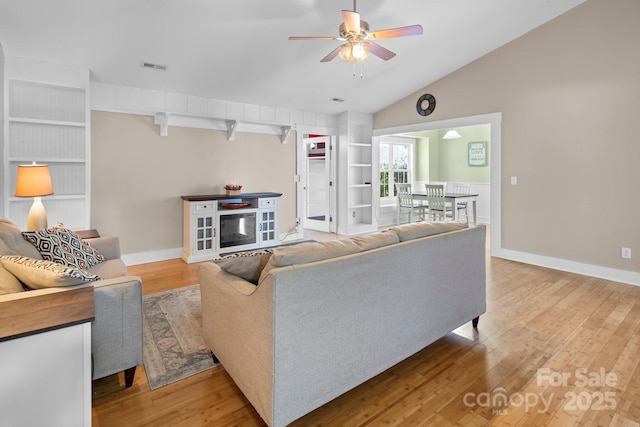 living area featuring lofted ceiling, visible vents, ceiling fan, built in shelves, and wood finished floors
