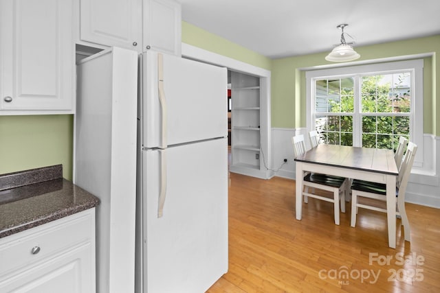 kitchen featuring dark stone countertops, freestanding refrigerator, light wood-type flooring, white cabinets, and wainscoting