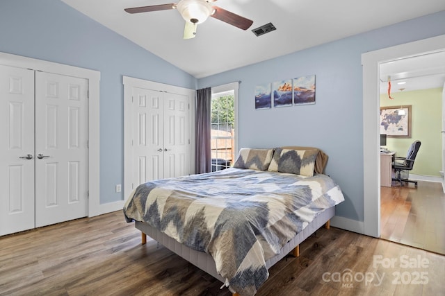 bedroom featuring vaulted ceiling, baseboards, visible vents, two closets, and wood finished floors