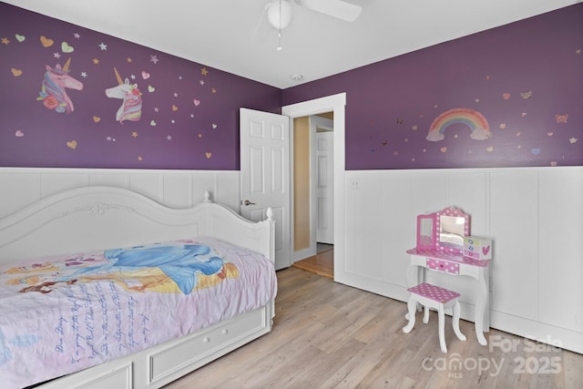 bedroom featuring ceiling fan, a wainscoted wall, wallpapered walls, and wood finished floors