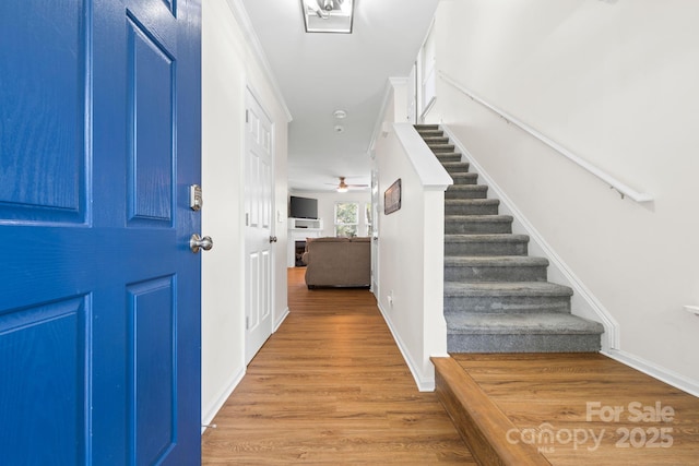 foyer entrance featuring baseboards, ceiling fan, wood finished floors, and stairs