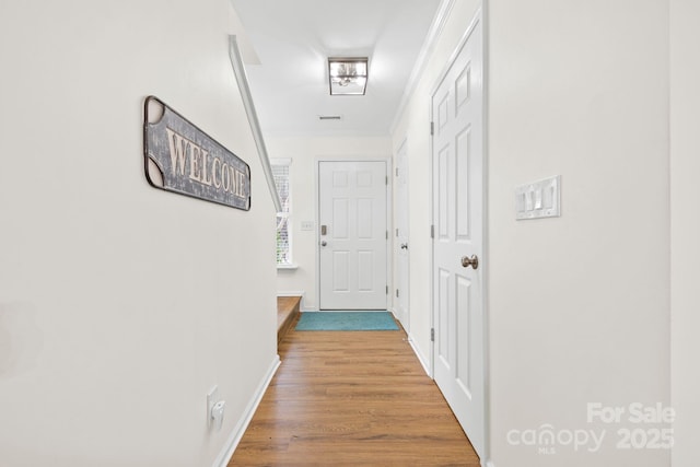 hallway featuring baseboards, ornamental molding, and wood finished floors
