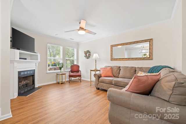 living room with a fireplace with flush hearth, light wood-style floors, a ceiling fan, and crown molding