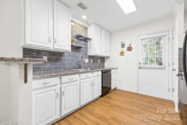 kitchen featuring visible vents, black dishwasher, a sink, light wood finished floors, and decorative backsplash