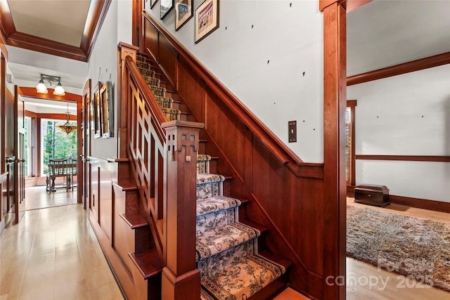 stairway featuring a chandelier, wood finished floors, and ornamental molding