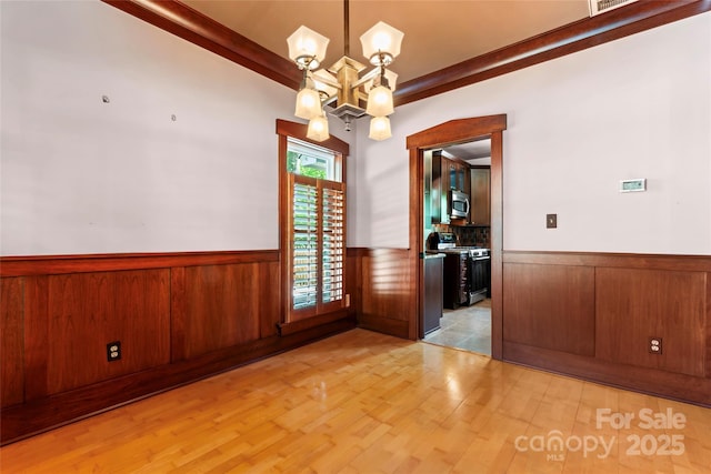 unfurnished room with a chandelier, light wood-style flooring, beamed ceiling, and a wainscoted wall