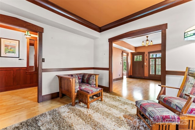 foyer entrance featuring wood finished floors, an inviting chandelier, ornamental molding, and a wainscoted wall