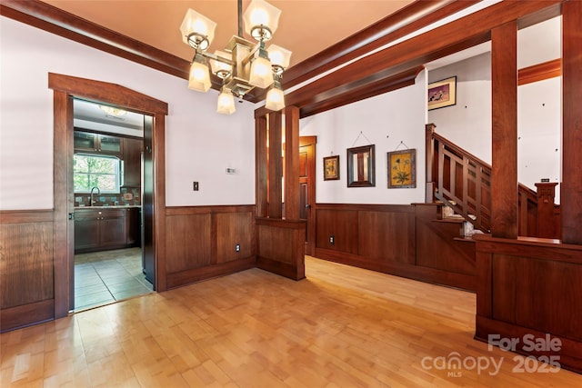 unfurnished dining area with wood finished floors, a sink, a notable chandelier, and a wainscoted wall