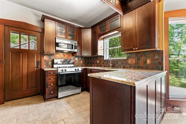 kitchen with stainless steel microwave, light stone counters, range with gas cooktop, decorative backsplash, and a sink