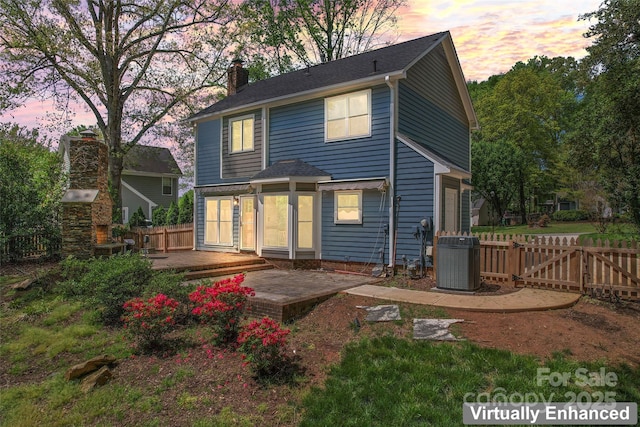 back of house at dusk featuring a patio area, central AC unit, fence, and a chimney