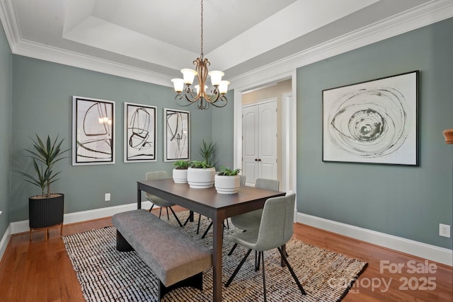 dining area with baseboards, wood finished floors, an inviting chandelier, and a raised ceiling