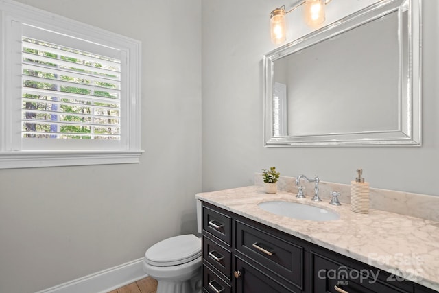 half bath featuring baseboards, wood finished floors, vanity, and toilet