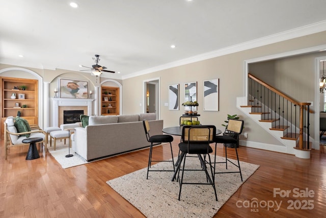 dining room with a ceiling fan, crown molding, built in shelves, a glass covered fireplace, and stairs