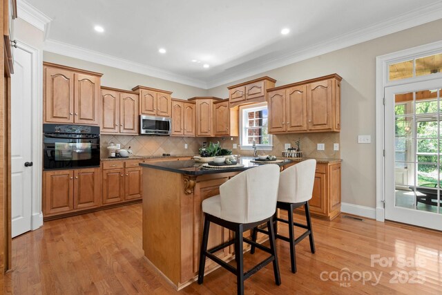 kitchen with stainless steel microwave, a kitchen bar, black oven, and light wood finished floors