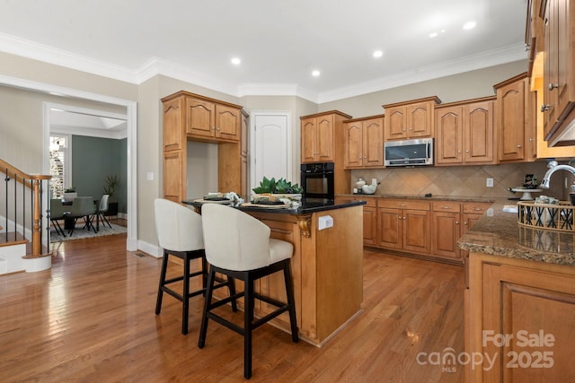 kitchen with stainless steel microwave, light wood-type flooring, a kitchen island, black oven, and a breakfast bar area