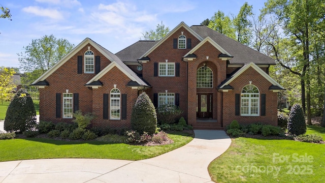 view of front of house with brick siding, a front yard, and roof with shingles