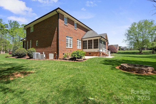 back of property with a lawn, a sunroom, brick siding, and central air condition unit
