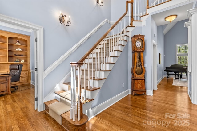 stairway featuring baseboards, a high ceiling, and wood finished floors