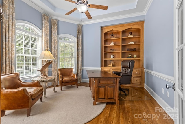 home office with baseboards, ornamental molding, a ceiling fan, a tray ceiling, and wood finished floors