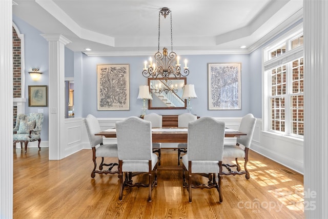 dining room with a tray ceiling, wood finished floors, an inviting chandelier, and a decorative wall