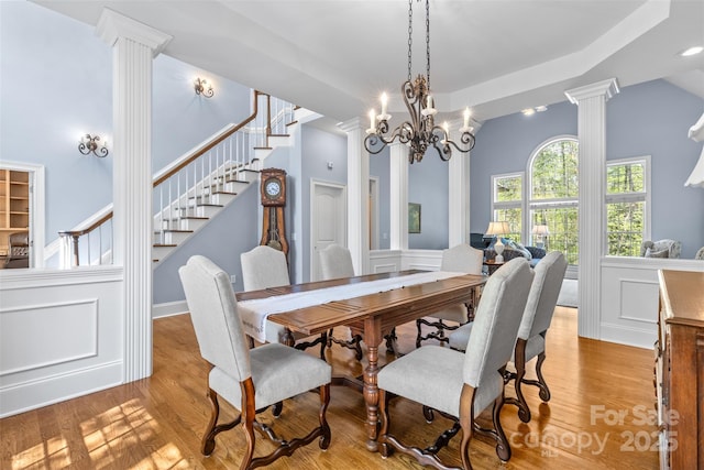 dining space with wood finished floors, decorative columns, a decorative wall, and stairs