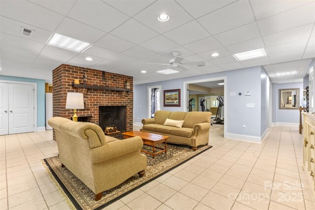 living room with a paneled ceiling, light tile patterned floors, a brick fireplace, and visible vents