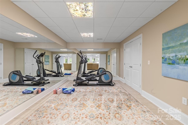 workout area with light tile patterned floors, a paneled ceiling, and baseboards