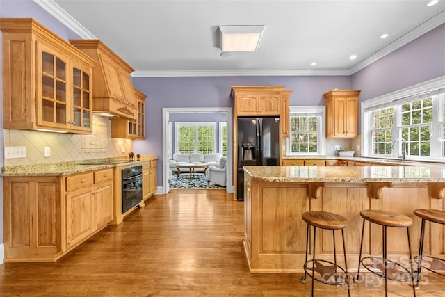kitchen with glass insert cabinets, a kitchen breakfast bar, black appliances, and light stone counters