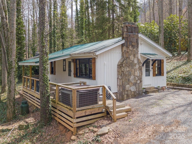 back of property with a wooded view, a chimney, metal roof, entry steps, and a deck