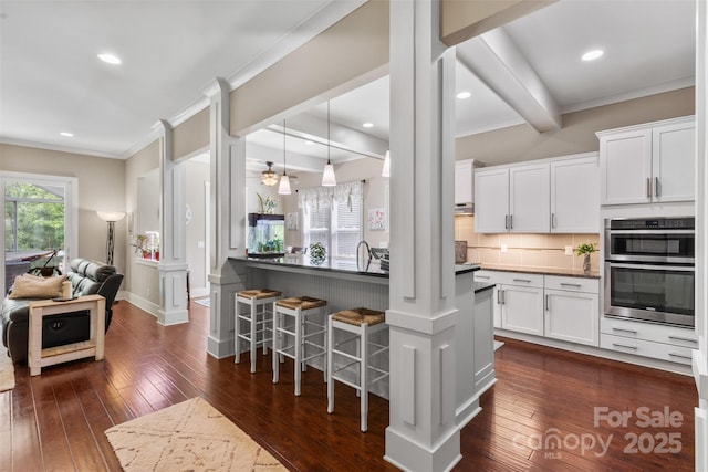 kitchen featuring crown molding, dark wood finished floors, double oven, and a breakfast bar