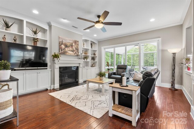 living room with crown molding, dark wood-style flooring, ceiling fan, and a fireplace with flush hearth