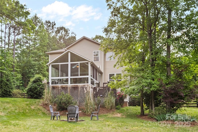 back of house featuring a lawn, a sunroom, and an outdoor fire pit