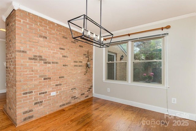 spare room with crown molding, baseboards, wood finished floors, brick wall, and an inviting chandelier