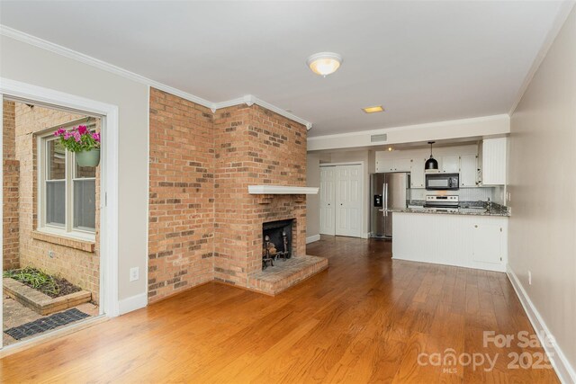 unfurnished living room featuring baseboards, wood finished floors, ornamental molding, and a brick fireplace